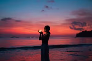 Mujer en la orilla del mar al atardecer sosteniendo una luz, imagen de la terapia de aceptación y compromiso con psicodélicos