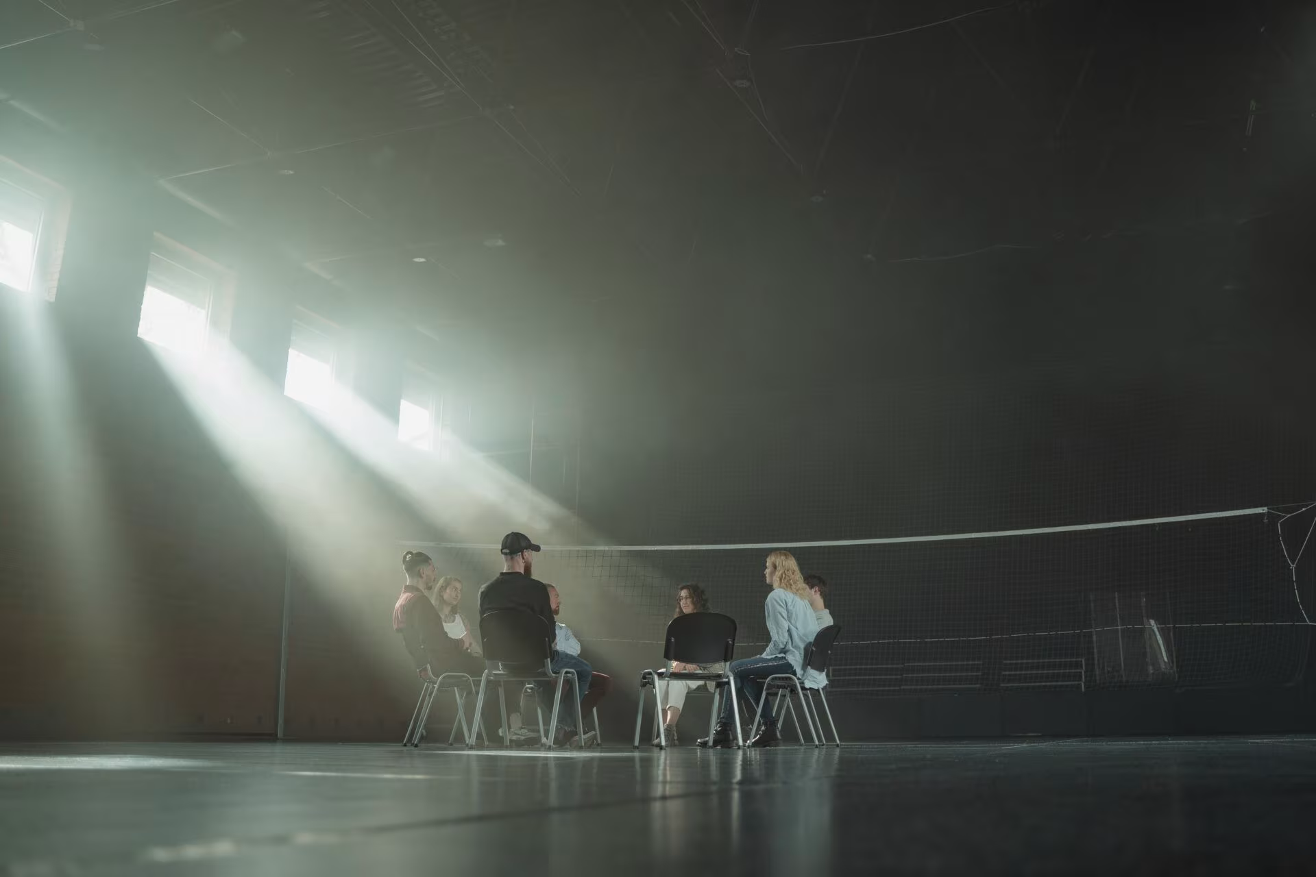 Grupo sentado en círculo en una sala oscura iluminada por haces de luz, en una sesión de integración psicodélica