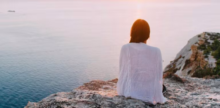 Mujer sentada de espaldas sobre una roca frente al mar, imagen del derivado de LSD para la ansiedad designado terapia innovadora por la FDA