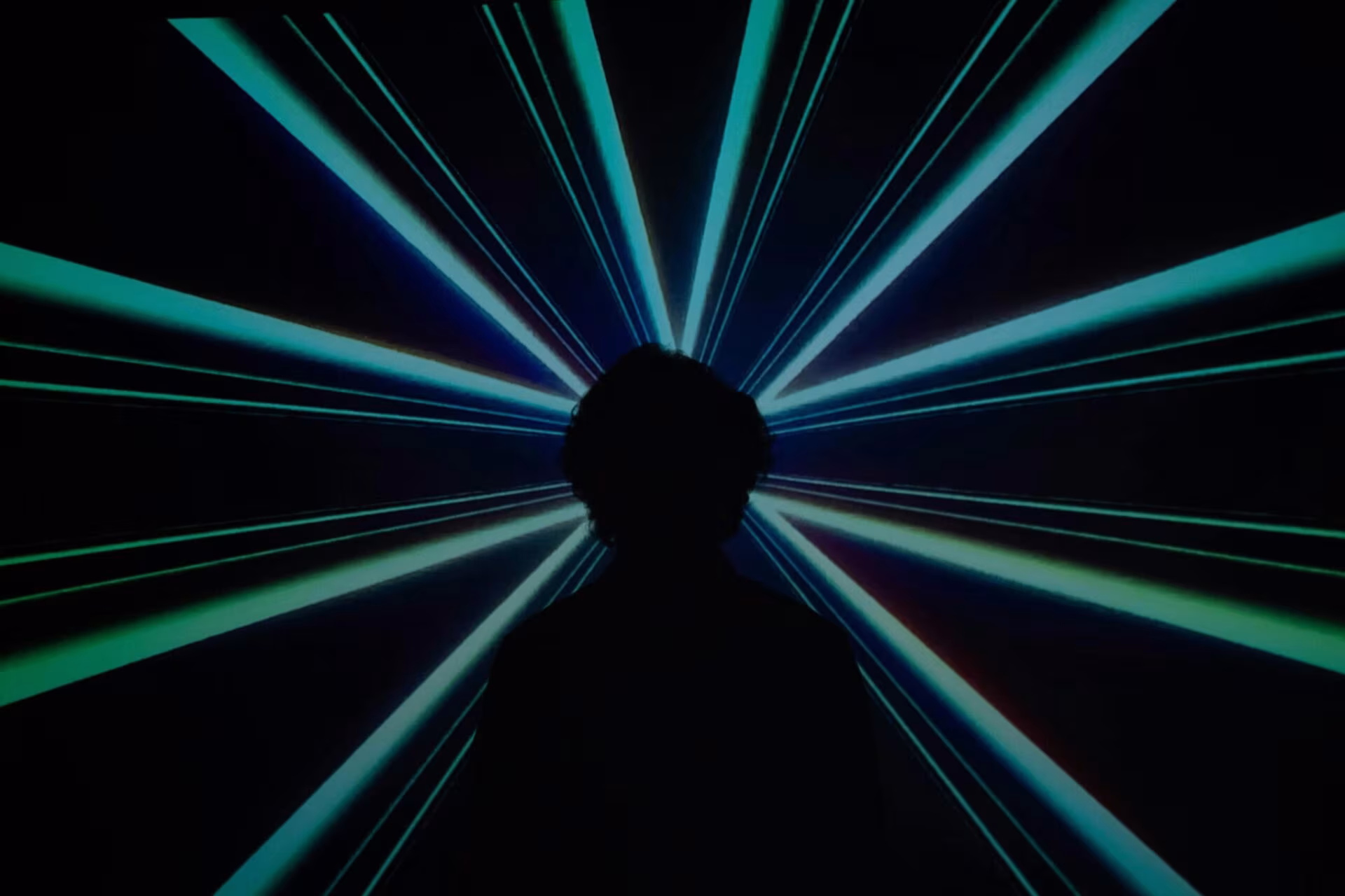 Silueta de una persona ante haces de luz verde azulada que irradian en la oscuridad, sobre el DMT y la visión