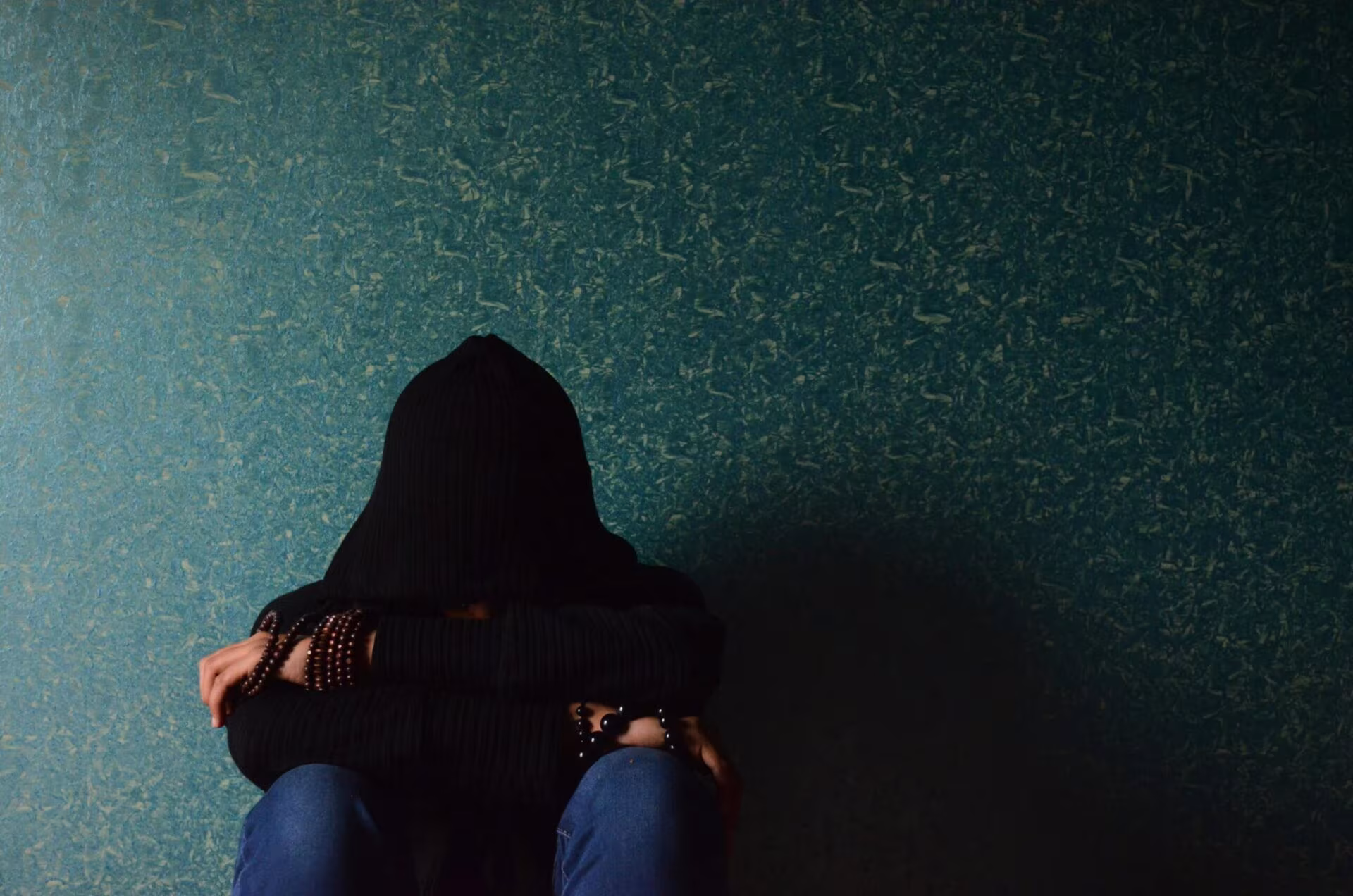 Persona encapuchada sentada con la cabeza entre las rodillas contra una pared verde, sobre microdosis de LSD y depresión