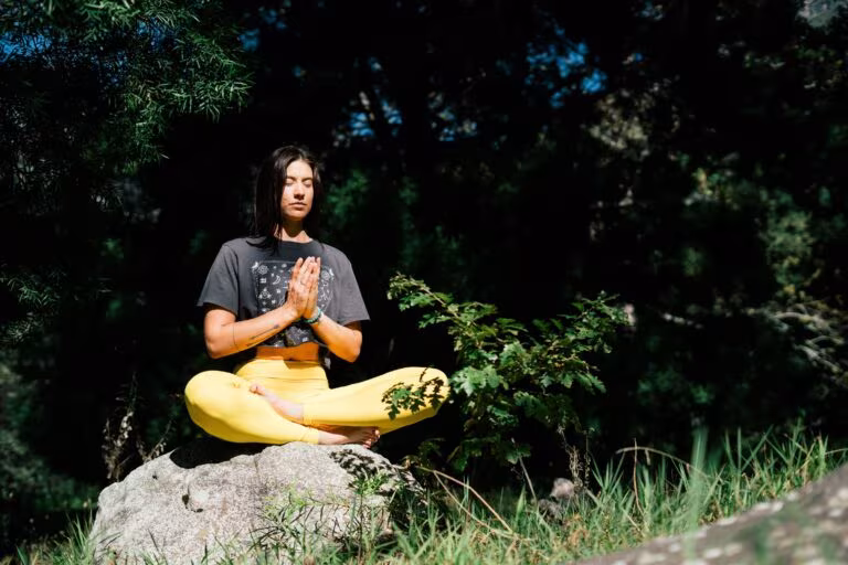 Mujer meditando sentada sobre una roca en un bosque, imagen de la meditación bajo los efectos de la DMT con harmina