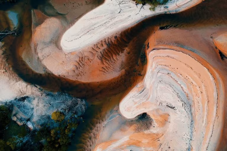 Vista aérea de formas sinuosas de arena y agua en tonos ocres, imagen de Inawe en el Parlamento Europeo con PsychedeliCare