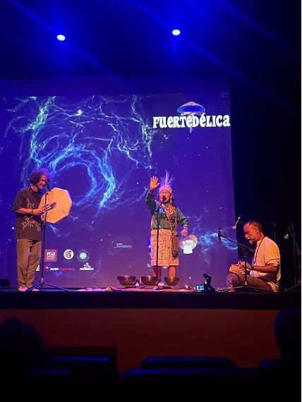 Músicos y una mujer con atuendo tradicional en el escenario de Fuertedélica 2025 con luces azules
