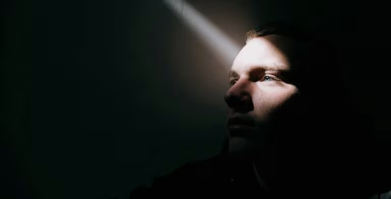 Rostro de una persona iluminado por un haz de luz en la oscuridad, imagen sobre el psicodélico GM-2505 para la depresión