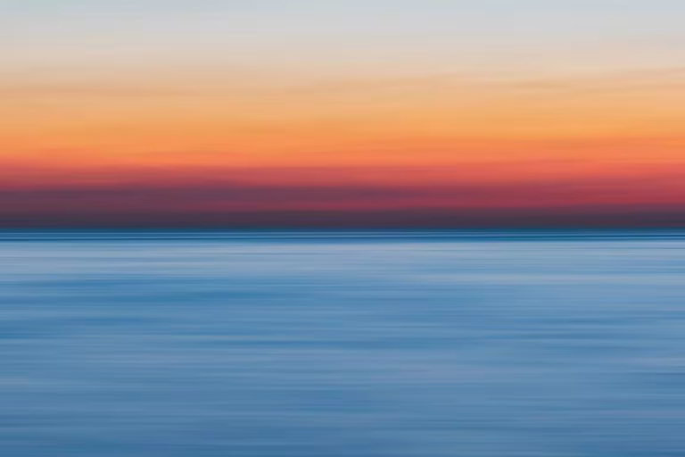 Horizonte del mar al atardecer en tonos naranjas y azules, imagen del metaanálisis sobre los efectos de la psilocibina